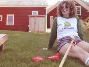 Woman sitting on the grass outside on a Summer's day, smiling with The Original Cornpole placed in her lap.